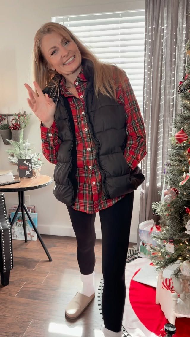 Woman wearing a red plaid shirt, black puffer vest, and black leggings indoors.