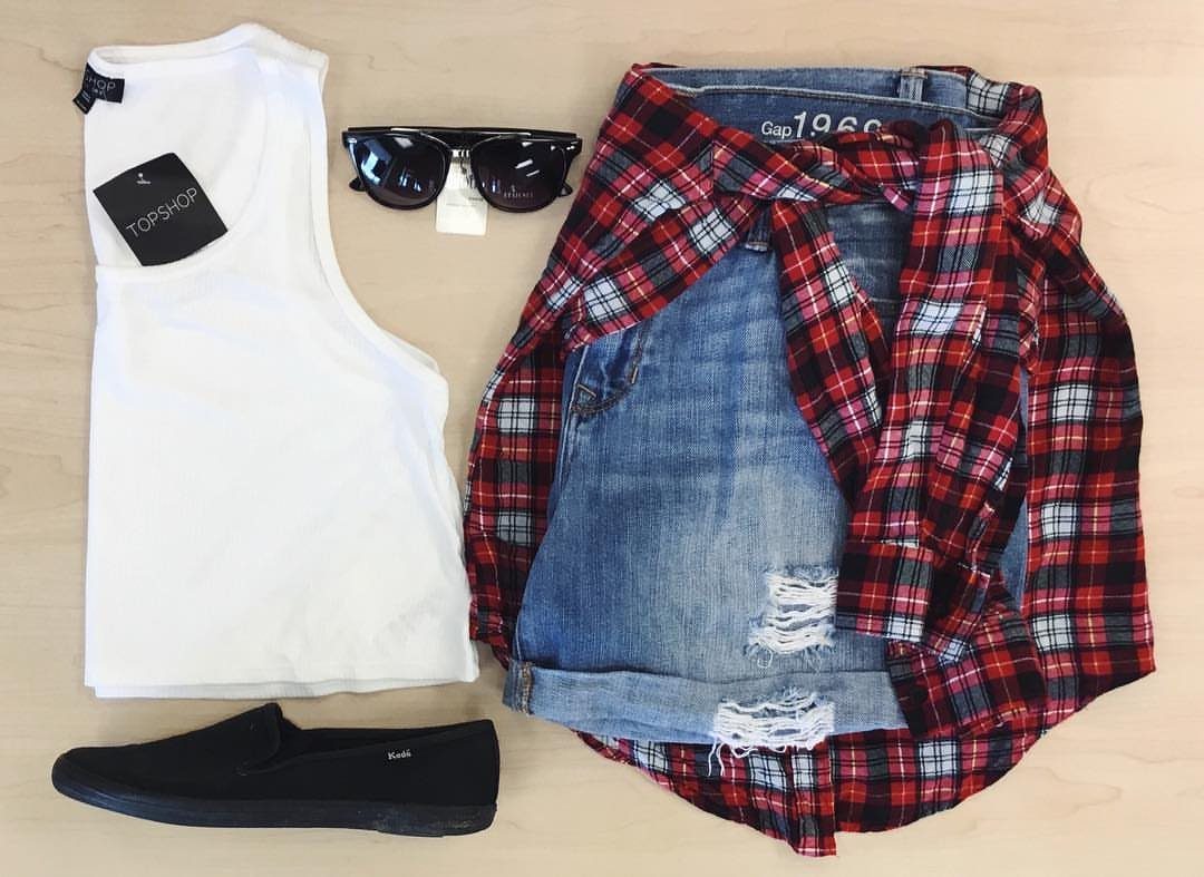 Red and black plaid shirt tied around blue distressed denim shorts flat lay.
