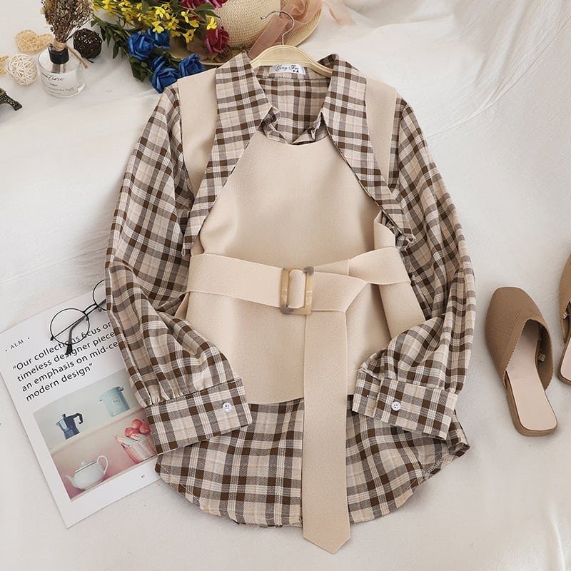 Brown plaid shirt layered under a beige belted pinafore dress on white background