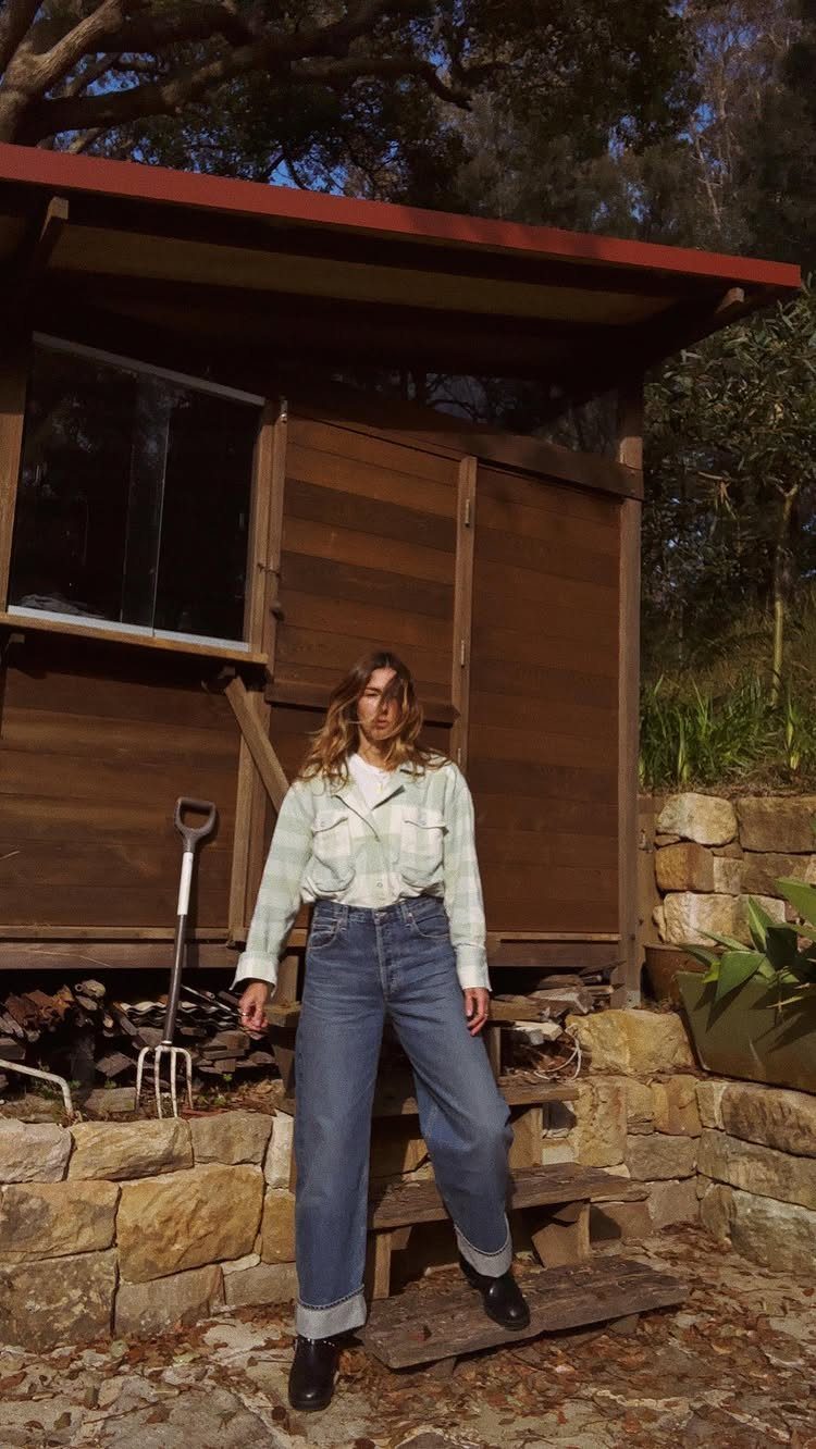 Woman wearing a light plaid shirt over a white t-shirt and blue jeans.
