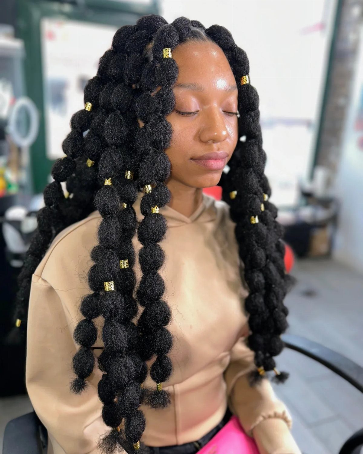 Woman with long black bubble braids decorated with gold metallic hair cuffs.