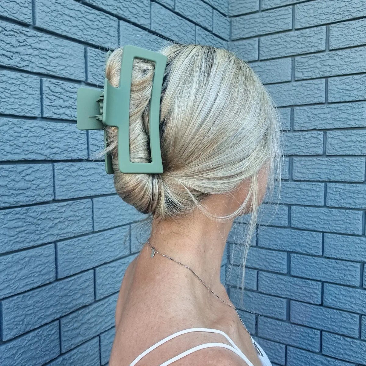 Blonde hair gathered in a bun held by a large sage green claw clip.
