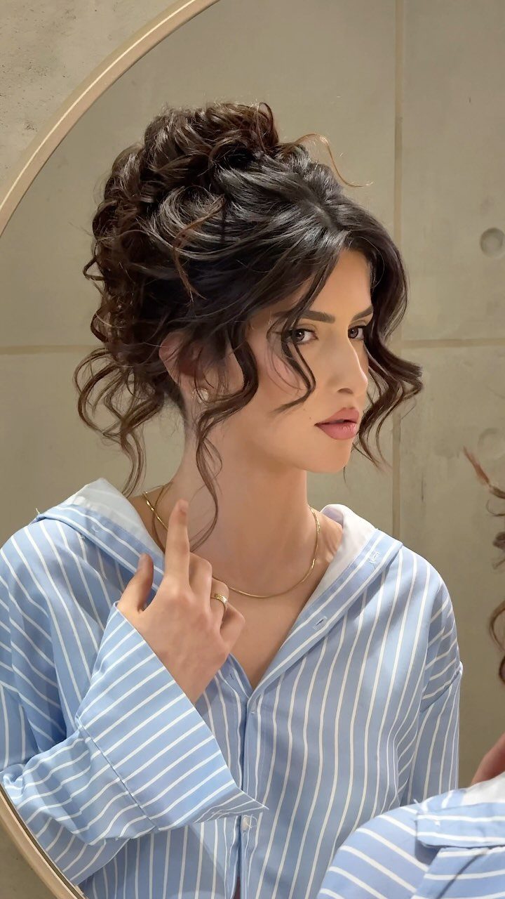 Woman with voluminous curly dark brown hair styled in a high poofy updo.