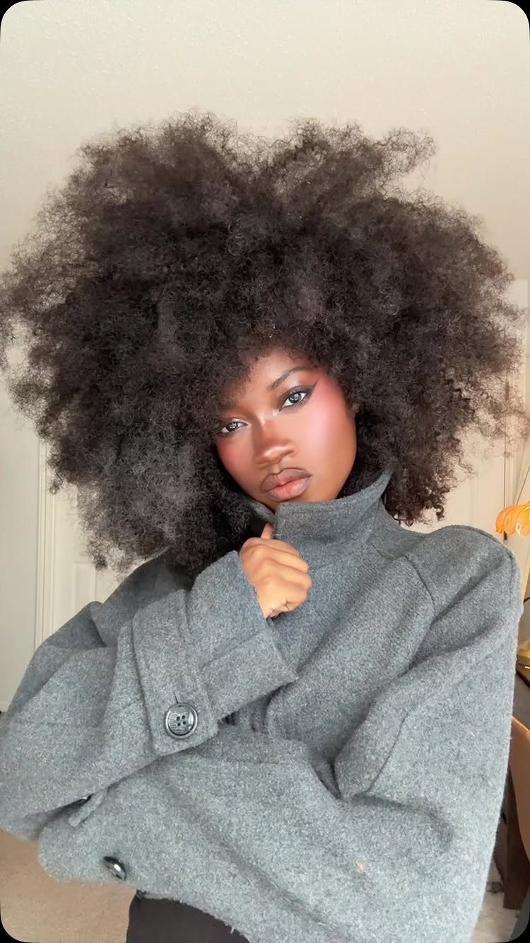 Woman with voluminous poofy black curly hair wearing a grey high-collar coat.
