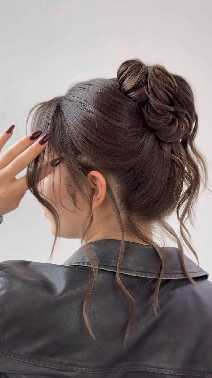 Woman with brown hair in a high twisted bun and loose curly tendrils.