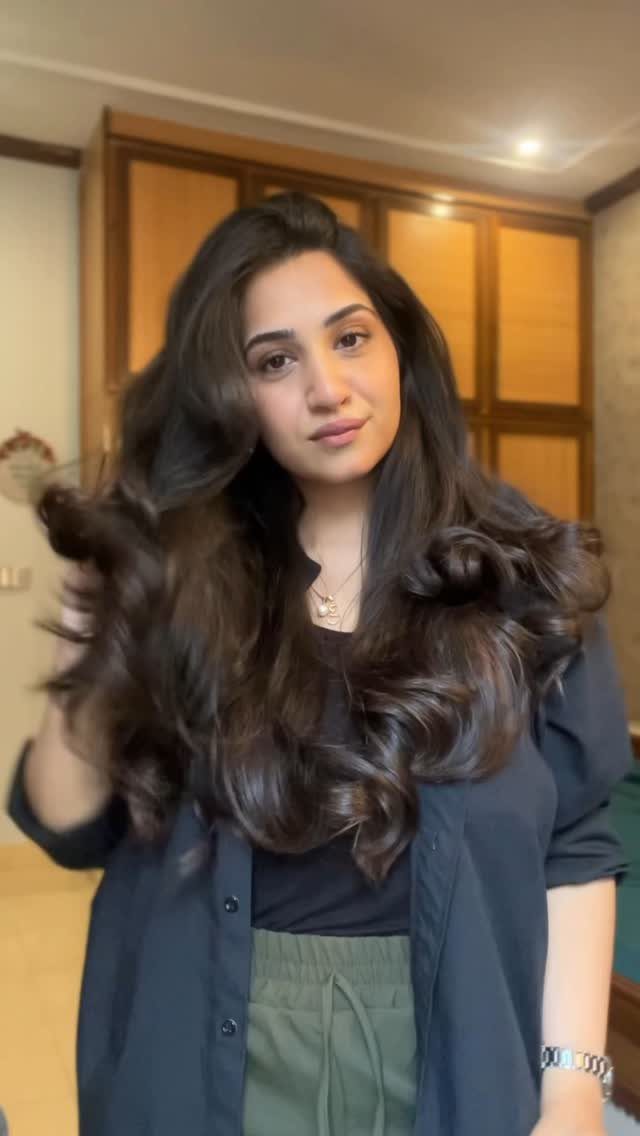 Woman with voluminous dark brown wavy hair posing in a room with wooden cabinets.