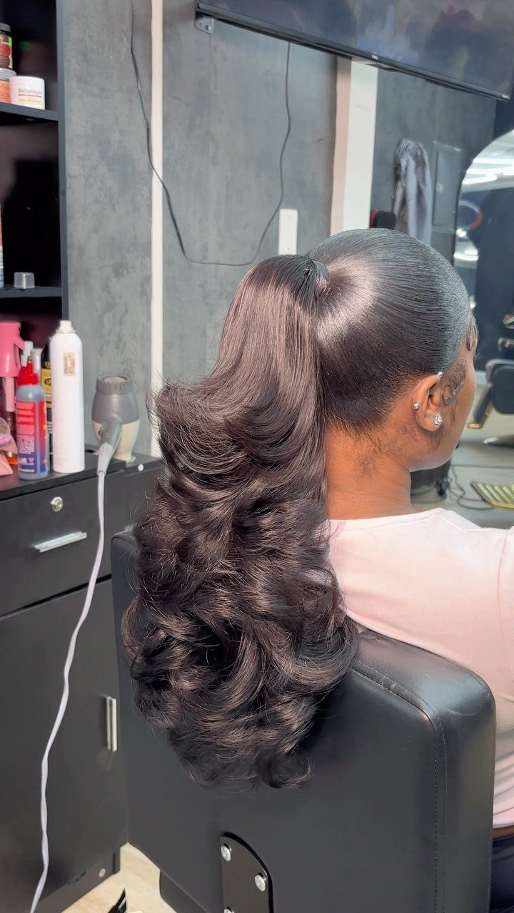 Woman with a slicked-back high ponytail and voluminous, curly dark hair in a salon.