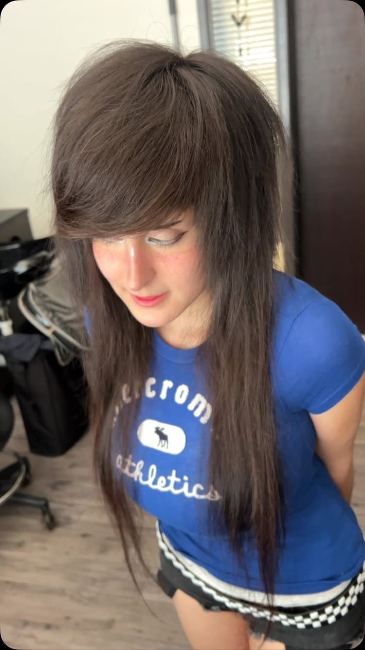 Woman with voluminous teased brown hair and long straight strands wearing blue shirt.
