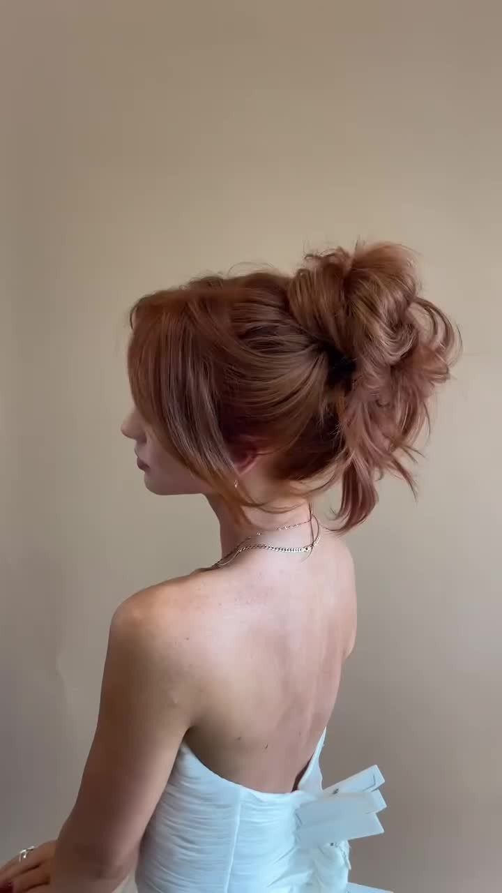 Woman with reddish-brown hair in a voluminous, tousled updo wearing a white dress.