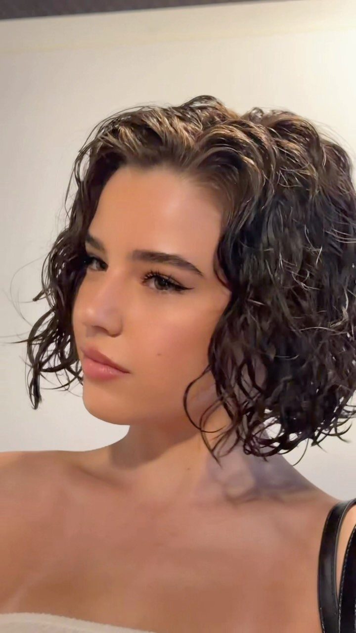 Woman with short, dark, curly hair styled in a glossy wet look.