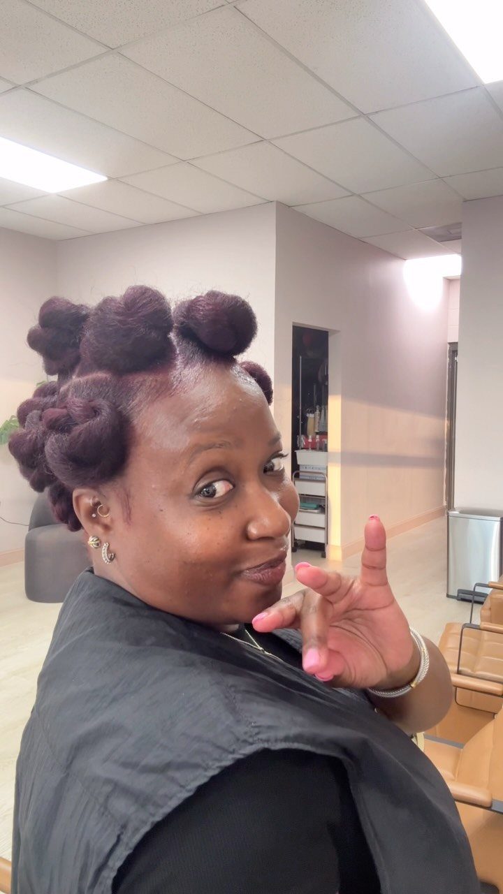Woman with dark hair styled in Bantu knots posing in a hair salon.