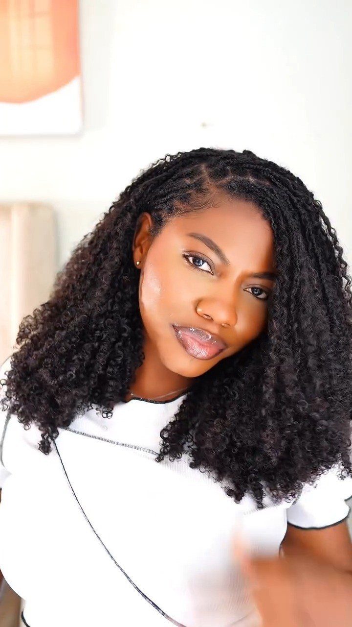 Woman with long curly black crochet braids wearing a white top.