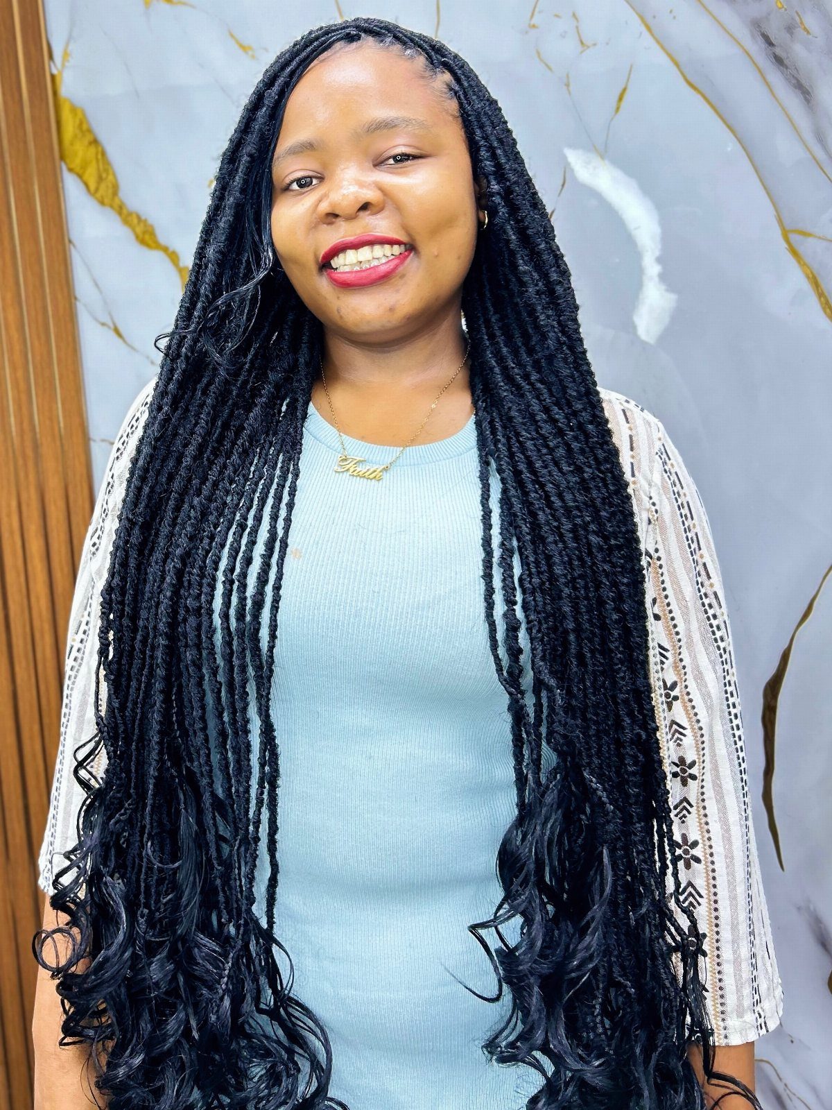 Woman with long black goddess locs and curly ends wearing a blue dress.