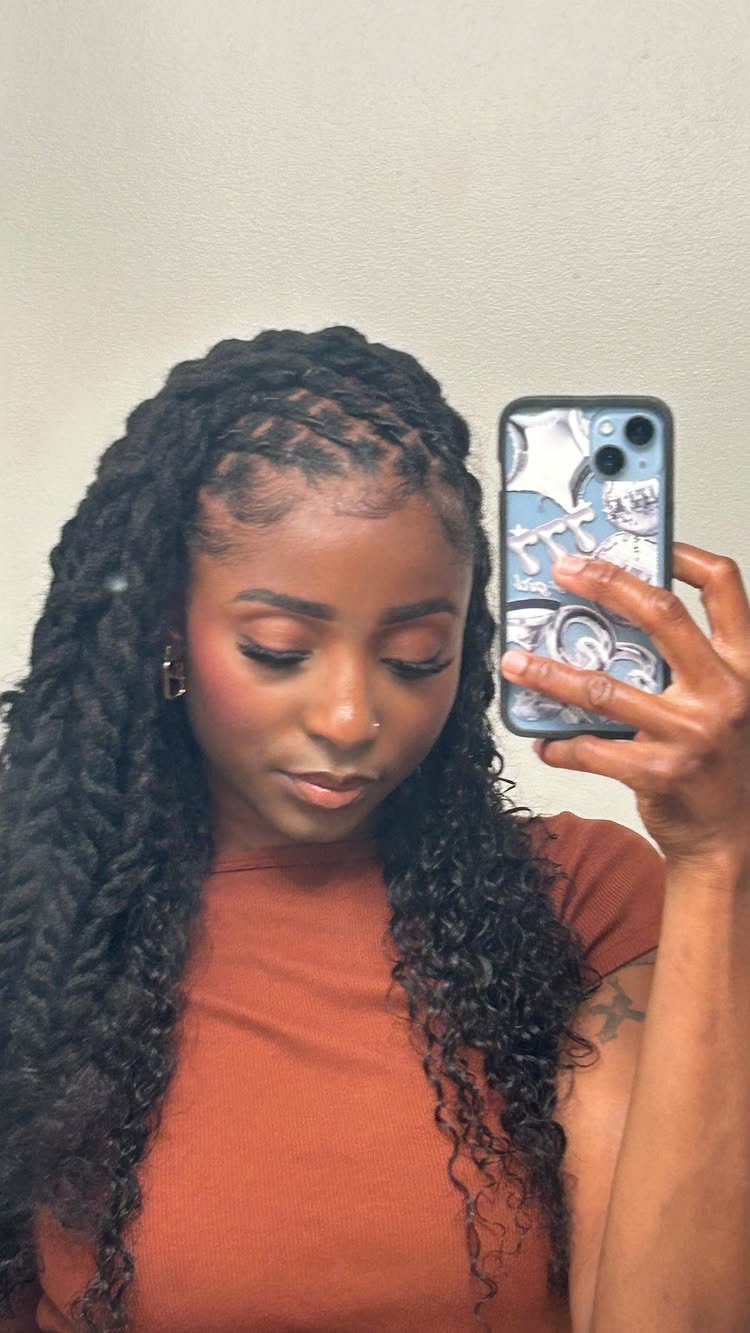 Woman with long dark twists taking a mirror selfie in a rust-colored shirt.