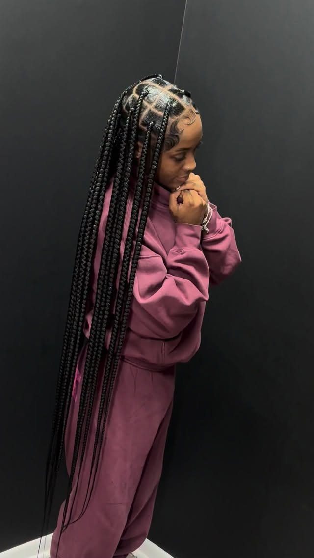 14 Protective Hairstyles with Braids and Twists to Try 7 Woman with long black box braids and square parts wearing a mauve tracksuit.