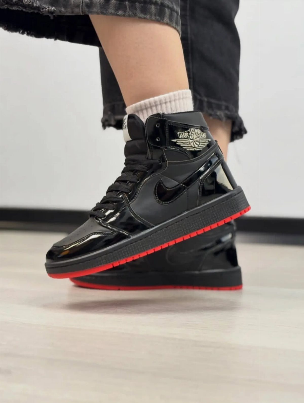 Glossy black high-top sneakers with red soles worn with black distressed jeans.