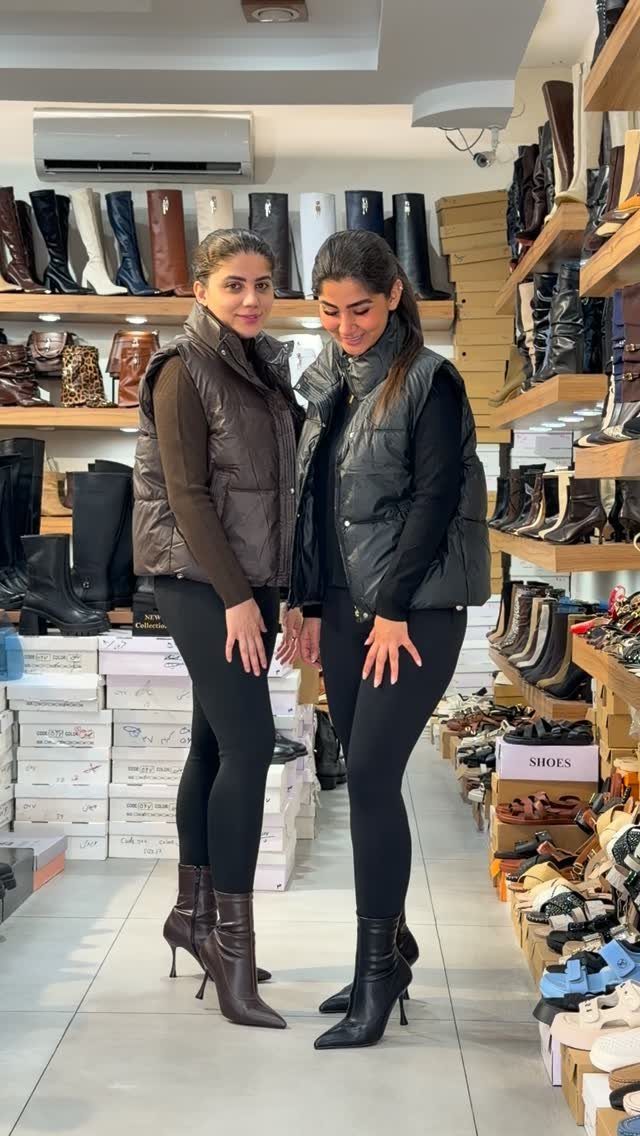 Two women wearing high-heeled ankle boots standing inside a shoe store.