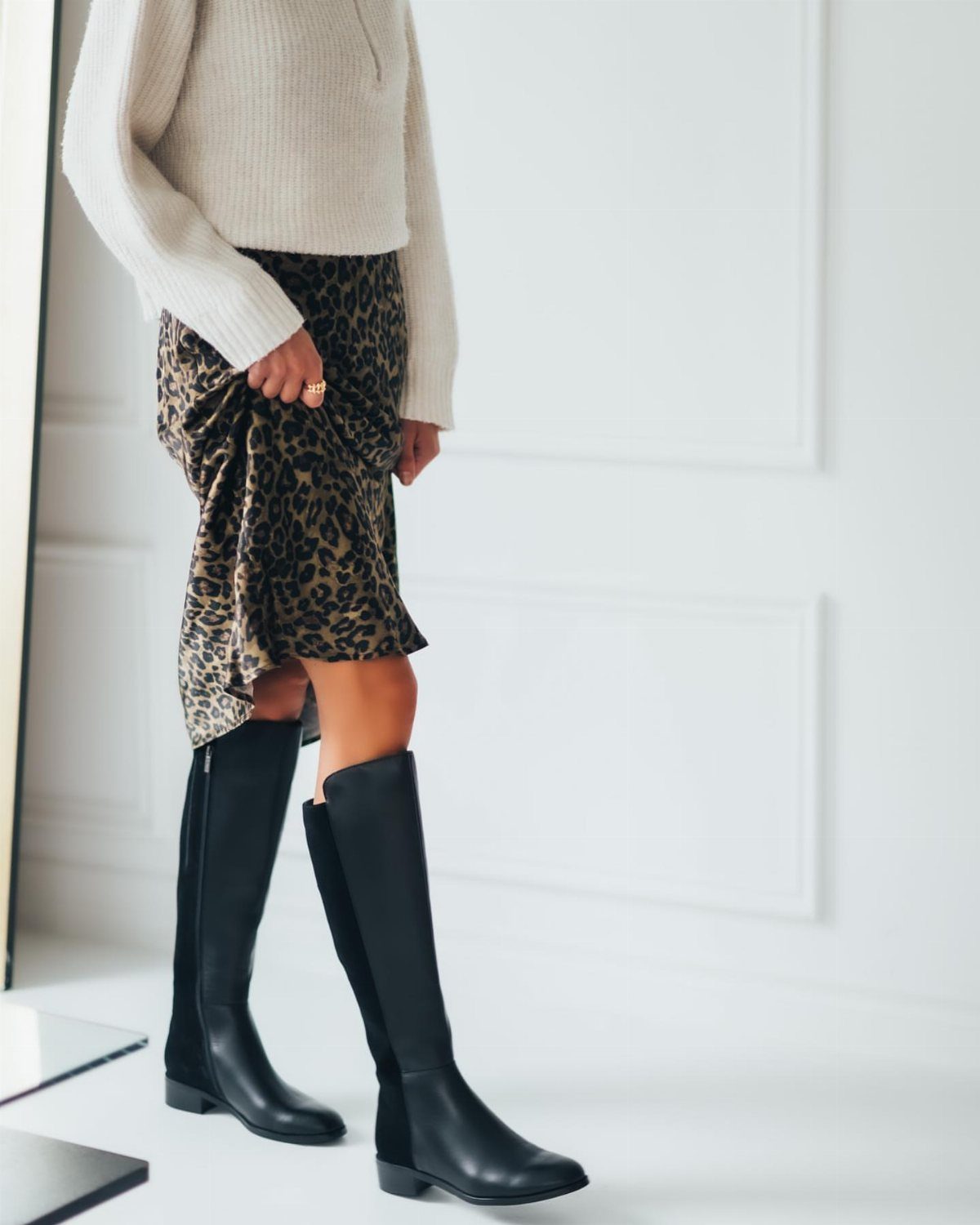 Tall black boots paired with a leopard print skirt and cream sweater.