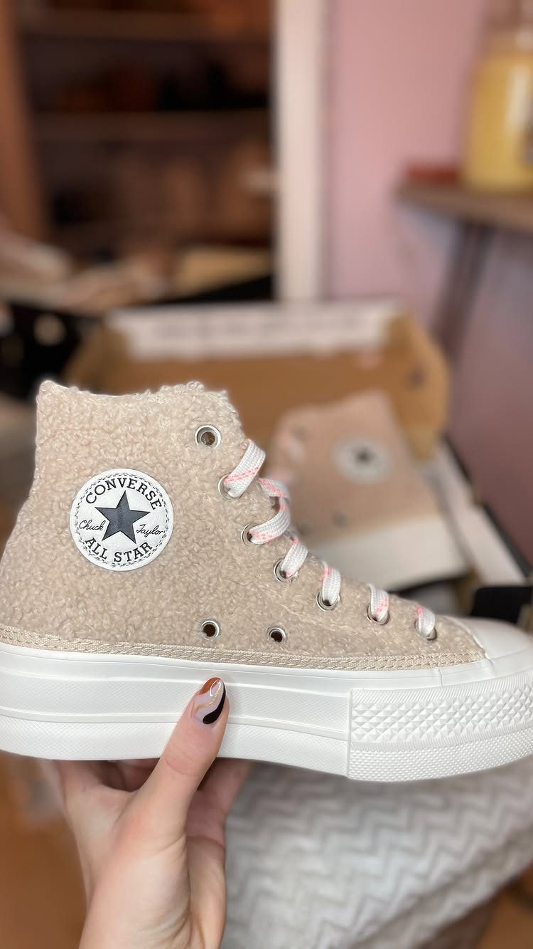 Beige fuzzy high-top Converse sneakers held by a hand against a blurred background.