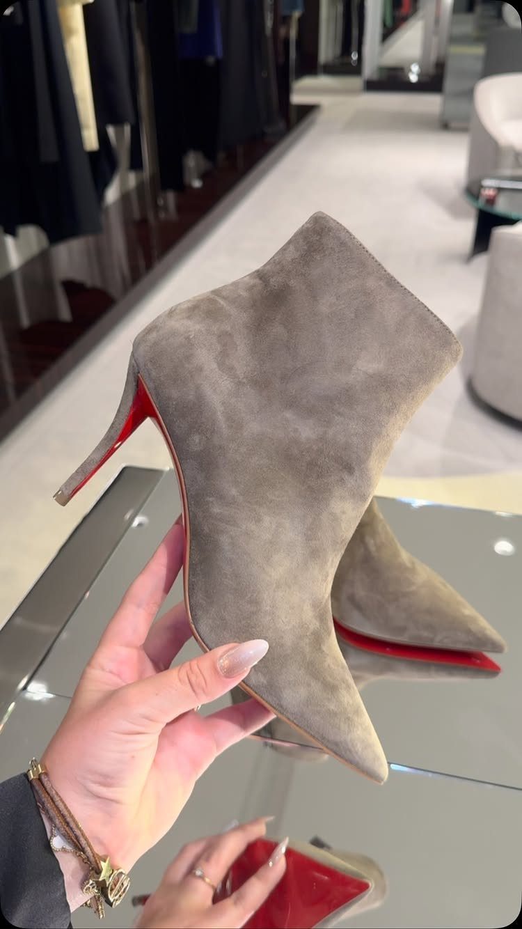 Grey suede pointed-toe stiletto ankle boots with red soles held in a hand.
