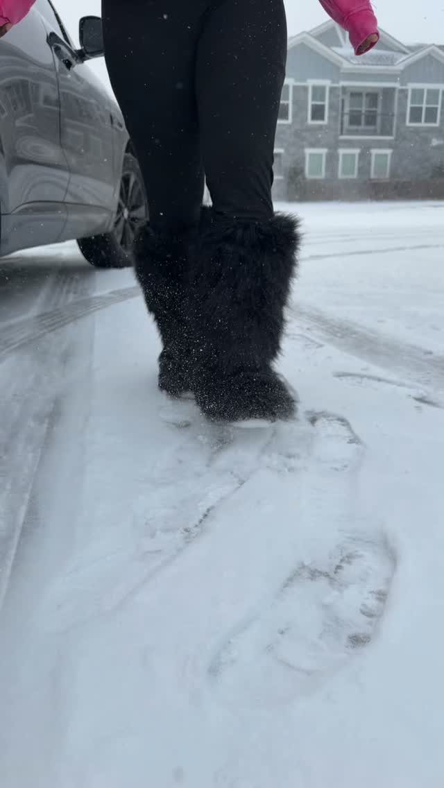 Black fluffy snow boots worn by a person standing in deep white snow.