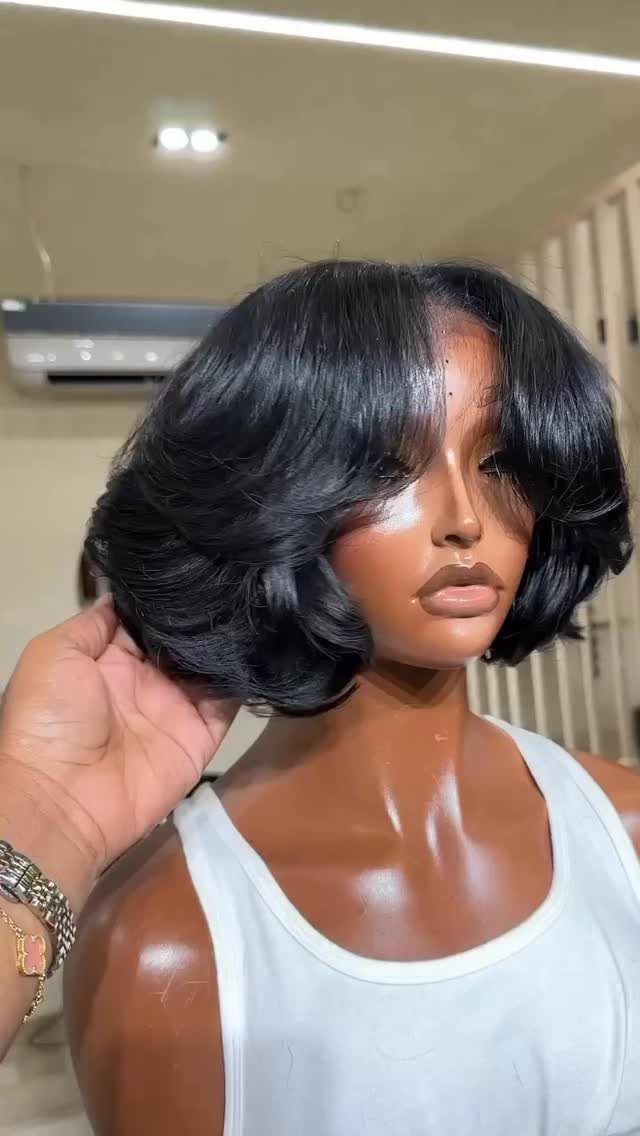 Person wearing a black bob wig with bangs and a white tank top.