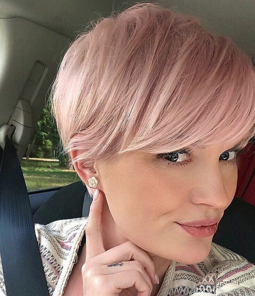 Woman with a pastel rose pink pixie cut hairstyle posing inside a car.
