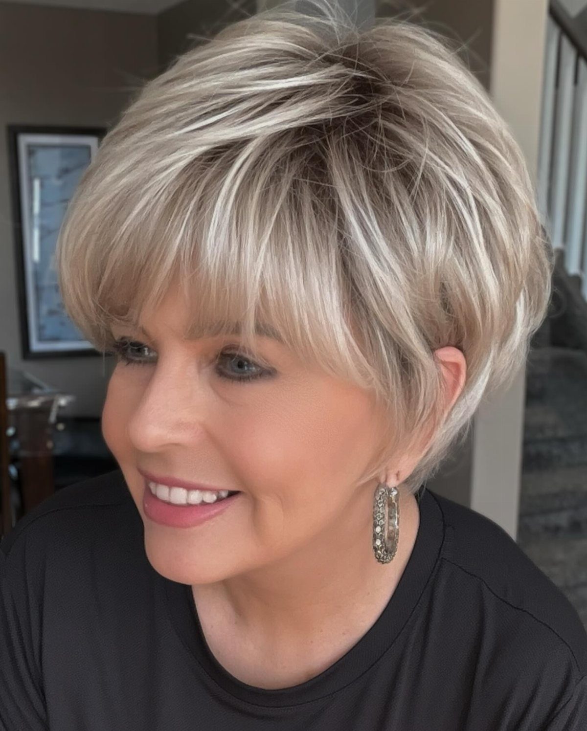 Woman wearing a short layered blonde wig with side-swept bangs and silver earrings.