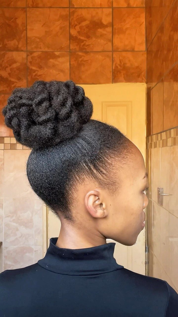 Black woman with a large twisted bun updo and a black turtleneck.
