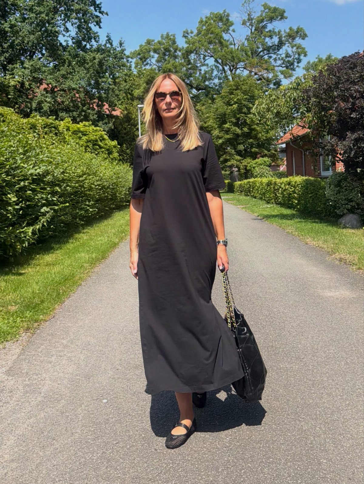 Woman wearing a black maxi dress and black flat shoes on a sunny path