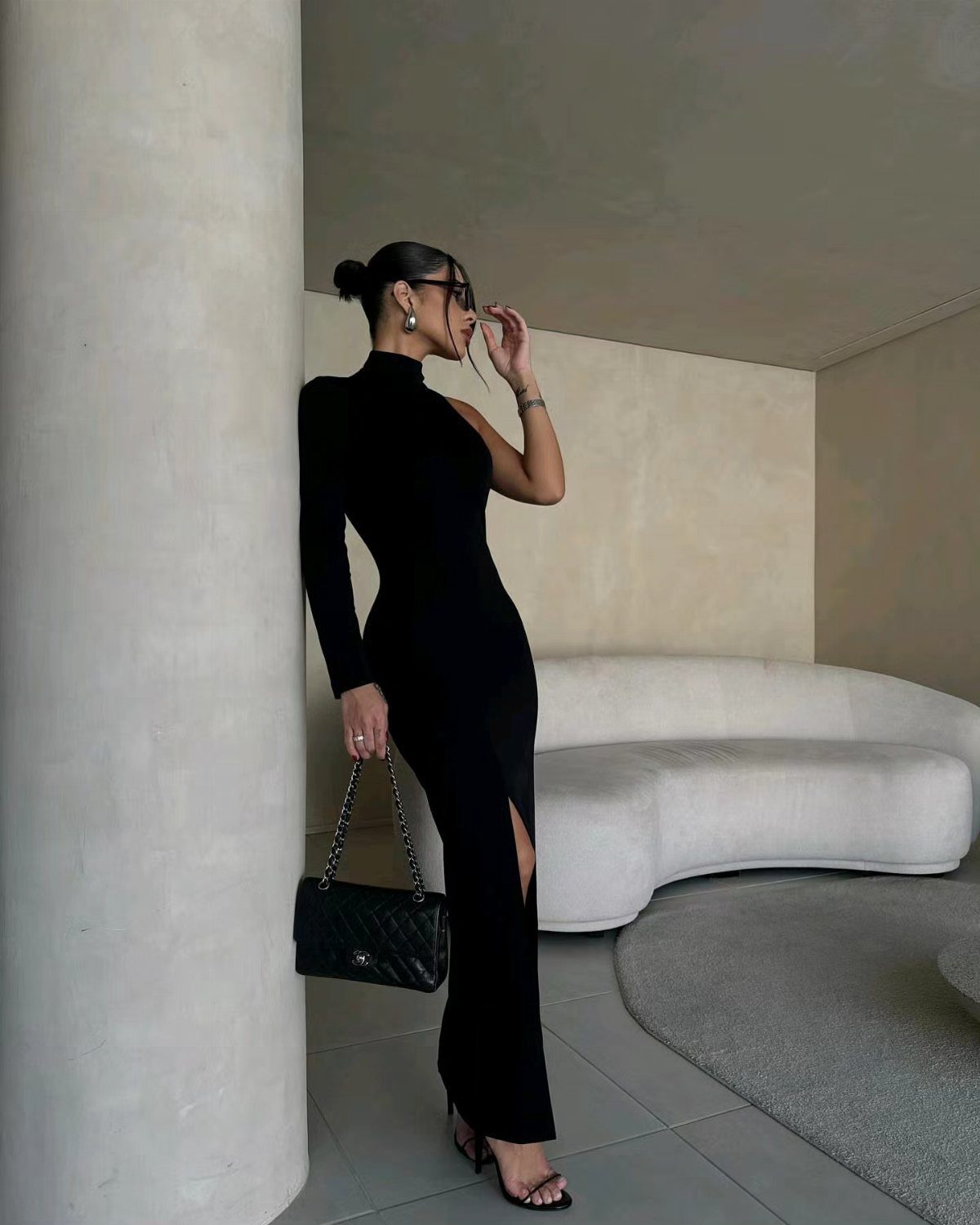 Woman in a one-shoulder black maxi dress wearing black strappy heeled sandals.
