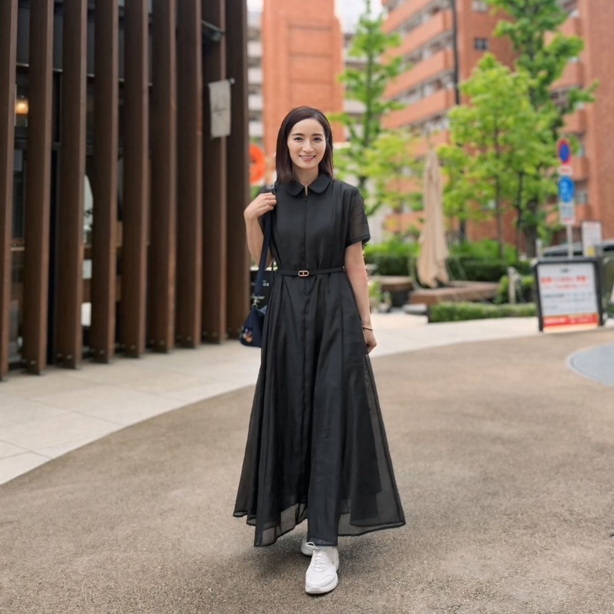 Woman in a black maxi dress with a skinny belt and white sneakers.