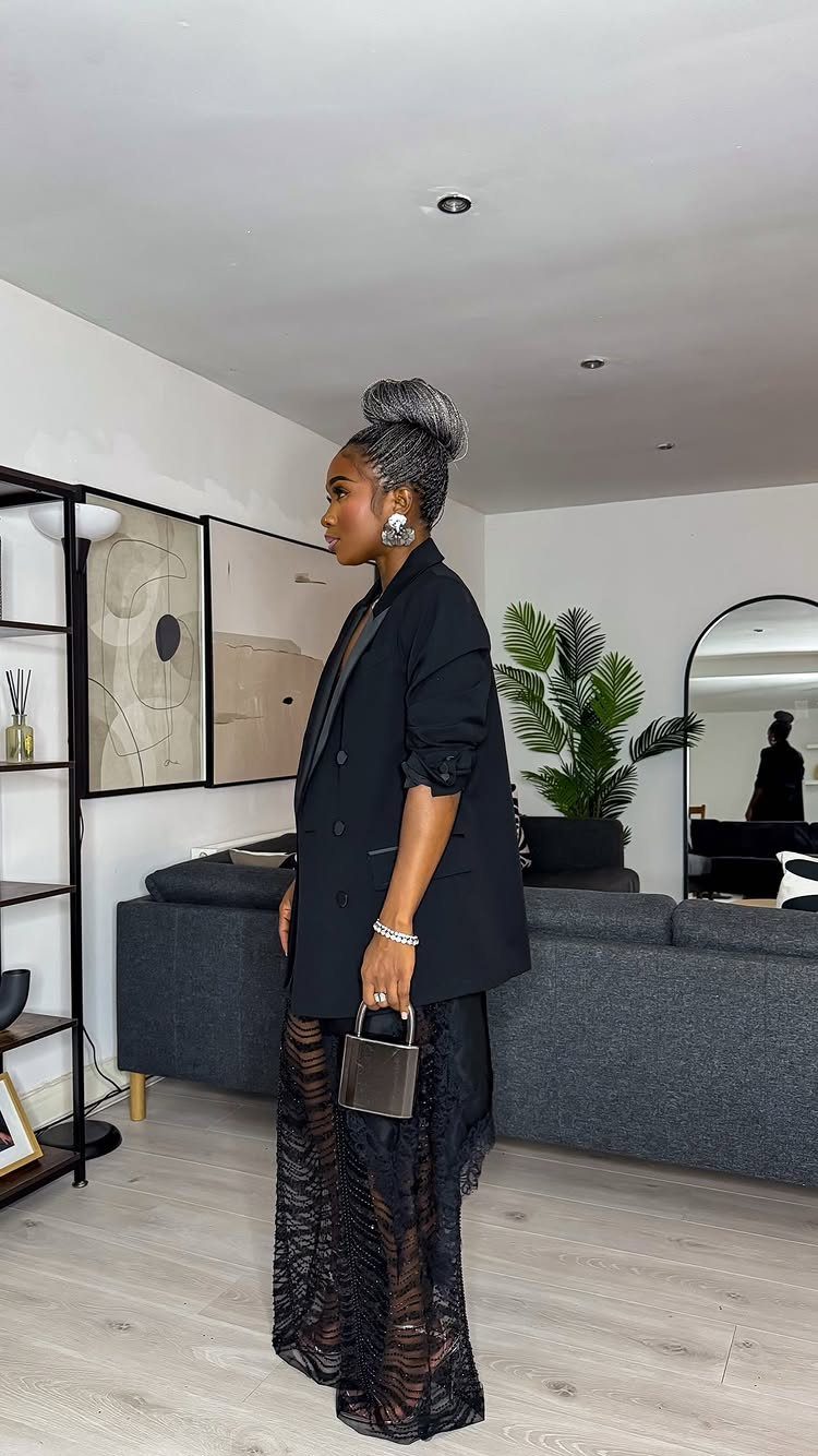Woman wearing a black lace maxi dress and blazer in a modern living room