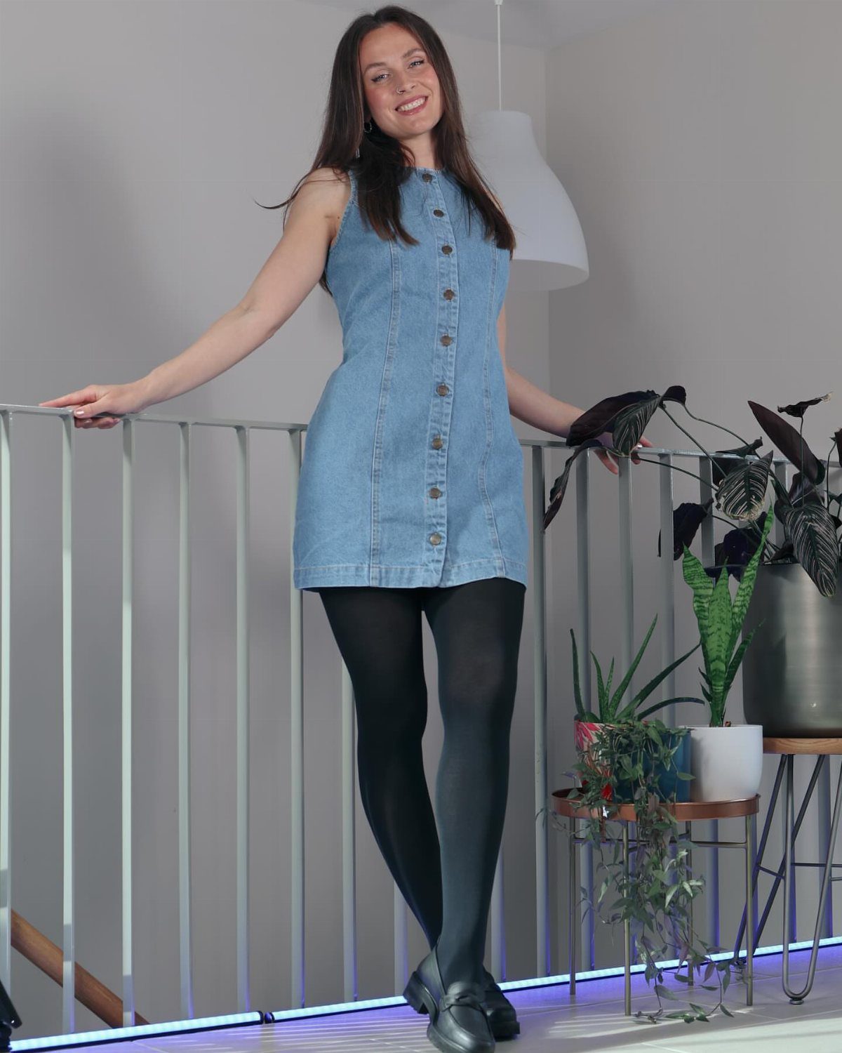 Woman wearing a blue denim mini dress with black opaque tights and shoes.