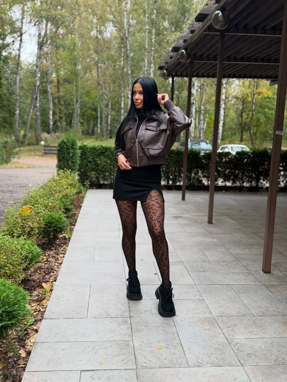 Woman wearing a brown leather biker jacket, black mini skirt, and patterned tights.