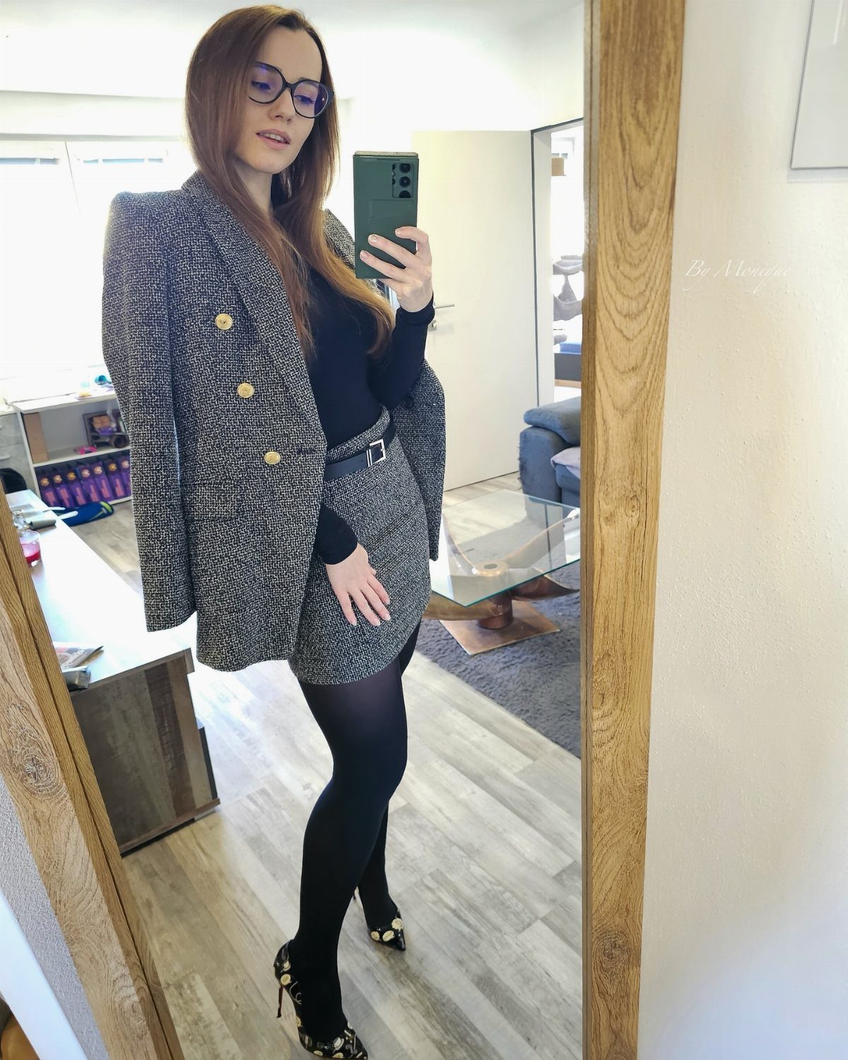 Woman in a grey tweed blazer and skirt set with black opaque tights.