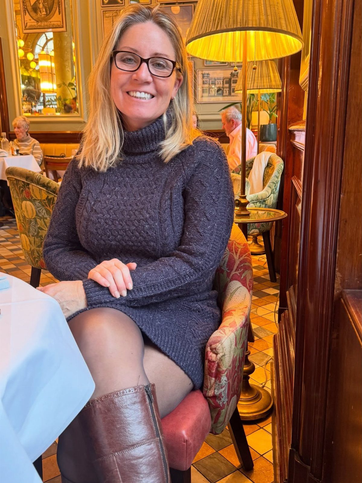 Woman wearing a grey turtleneck sweater dress with black tights and brown boots.