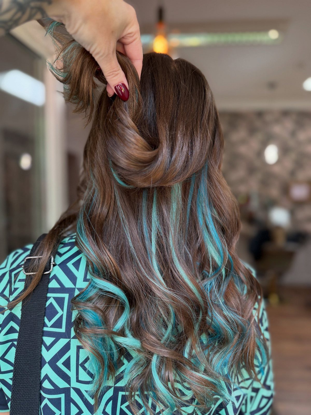Brown wavy hair lifted to show hidden turquoise blue highlights underneath.