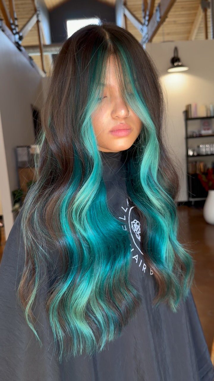 Person with long wavy brown hair and thick turquoise blue streaks framing the face