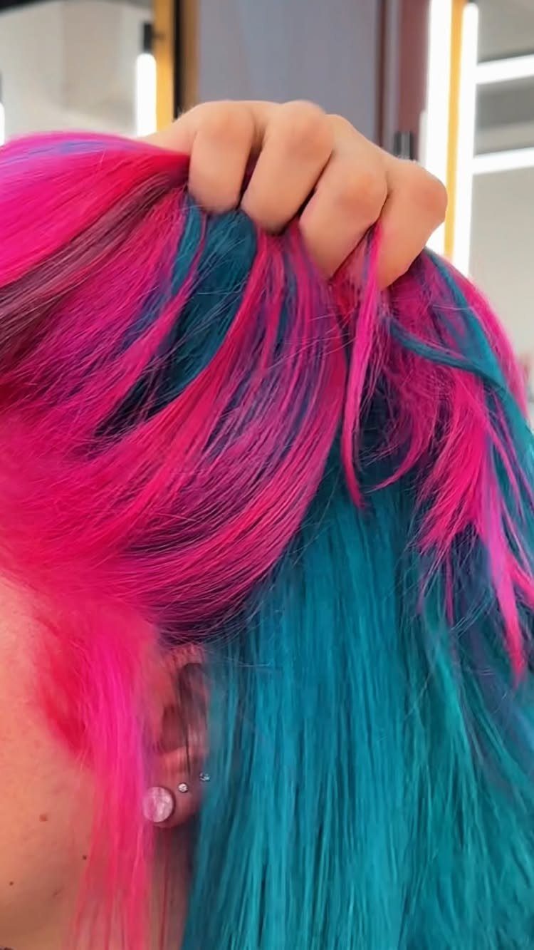 Vibrant pink and turquoise hair streaks with a hand lifting the top layer.