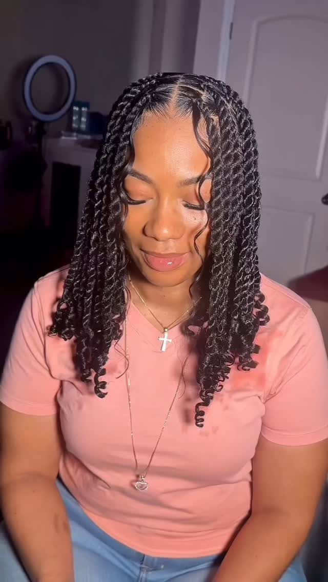 Woman with long black two strand twist hairstyles wearing a pink t-shirt.
