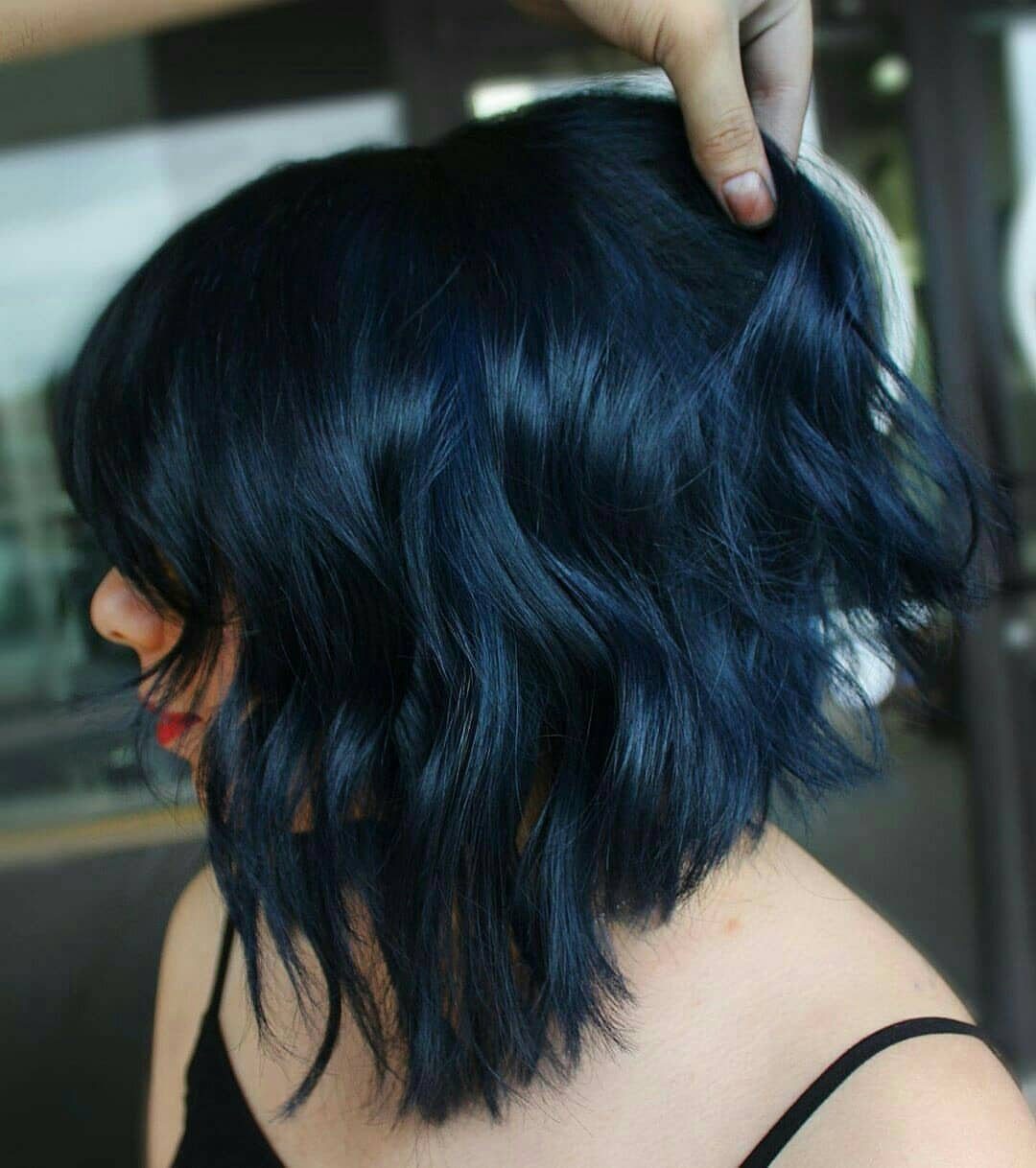 Types of Hair Colour: 12 Ideas, From Balayage to Copper 5 Wavy shoulder-length hair dyed a deep blue-black color held by a hand.