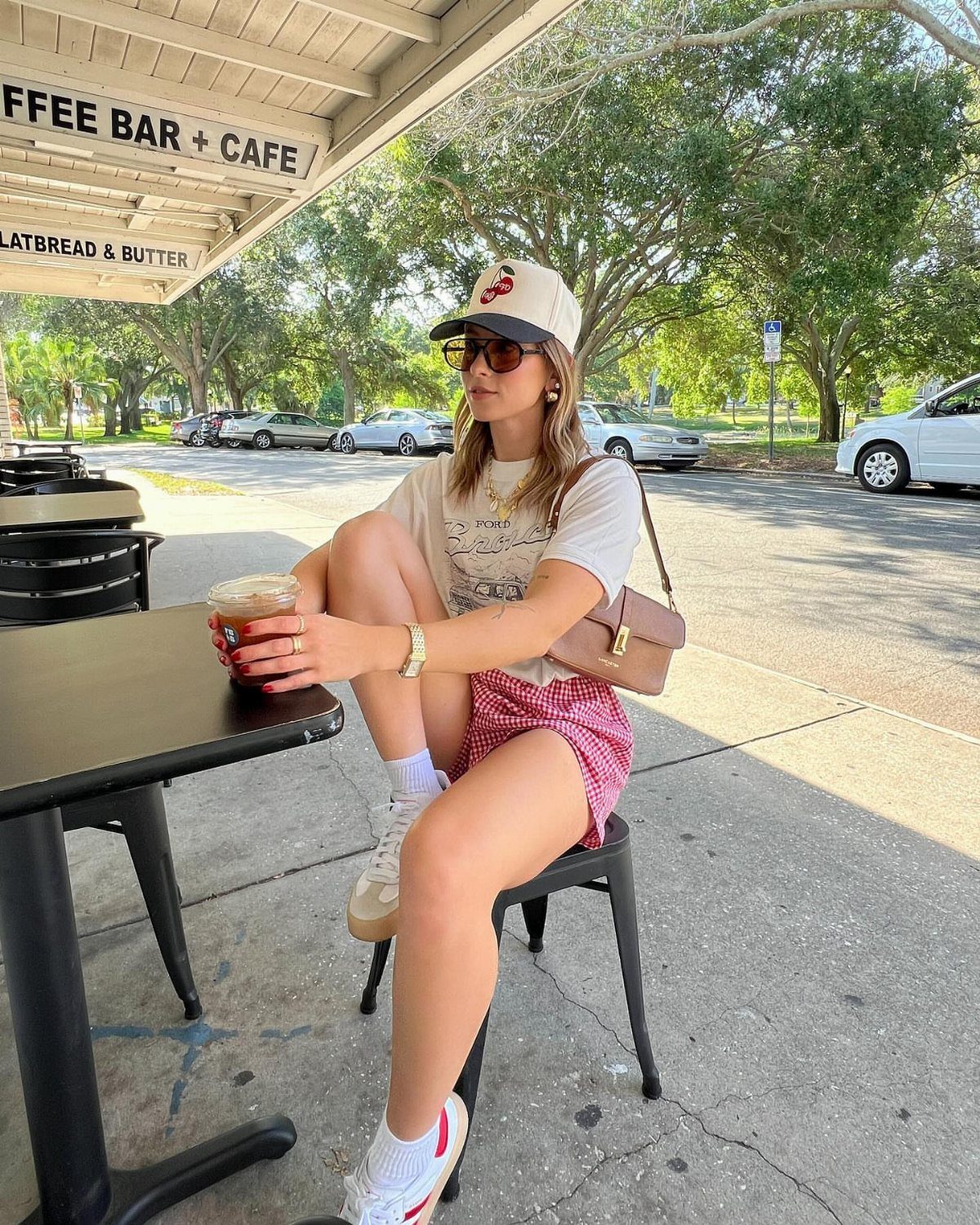 Woman wearing a white t-shirt and red patterned shorts sitting at a cafe.