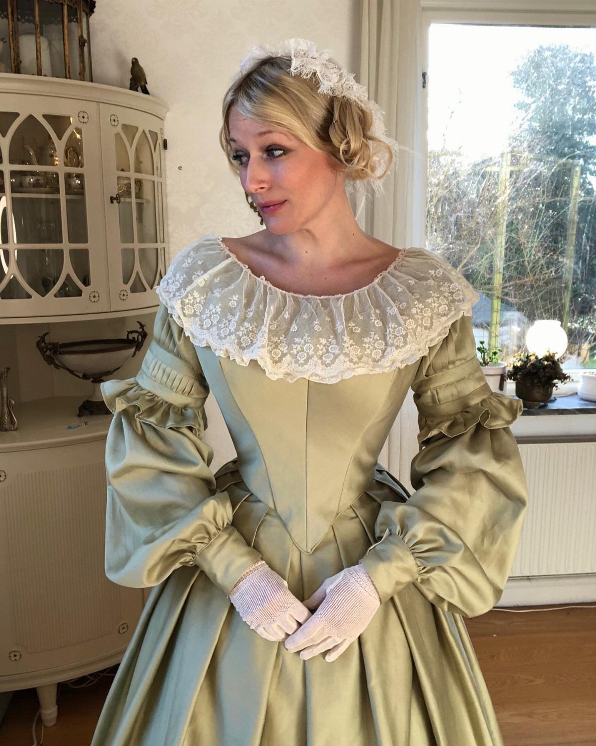 Woman in a light green satin Victorian gown with lace collar and gloves.