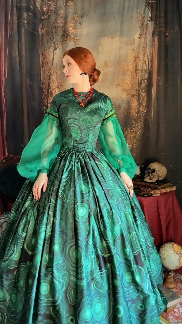 Woman in a voluminous iridescent green Victorian gown standing before a painted backdrop.