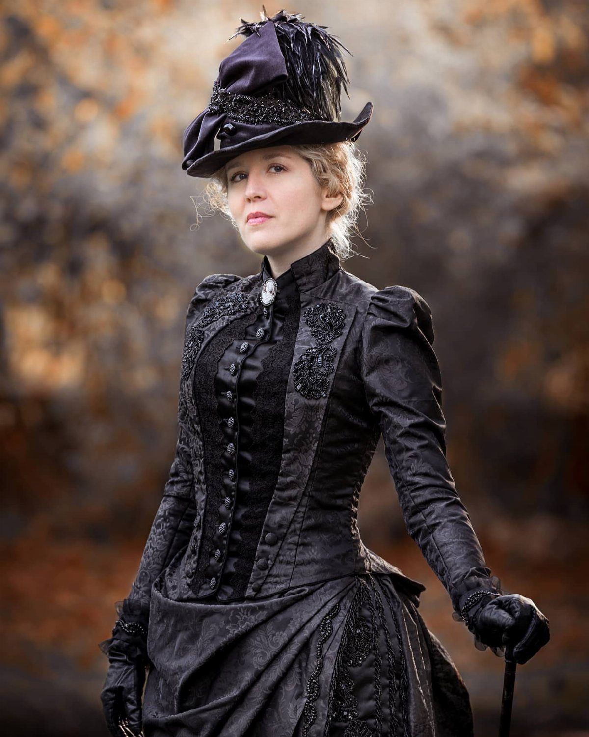 Woman in a black Victorian mourning dress and feathered hat in autumn woods
