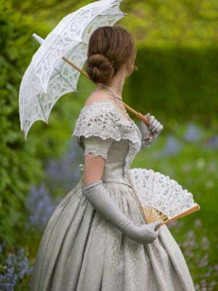 Woman in silver Victorian gown holding a white lace parasol and lace fan.