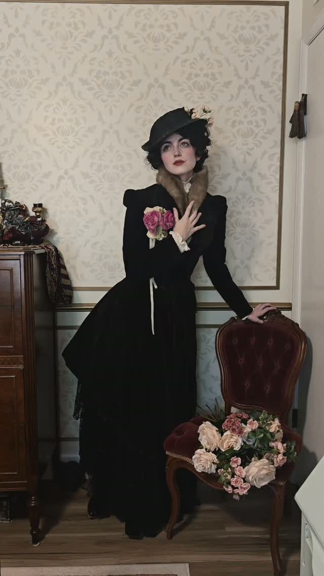Woman in a black Victorian royal dress and hat standing in a vintage room
