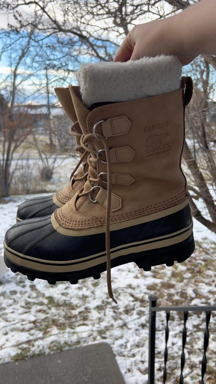 Winter Boots 2026: 8 Styles, From Slouchy to Shearling 2 Sorel Caribou waterproof boots in tan and black held against a snowy landscape.